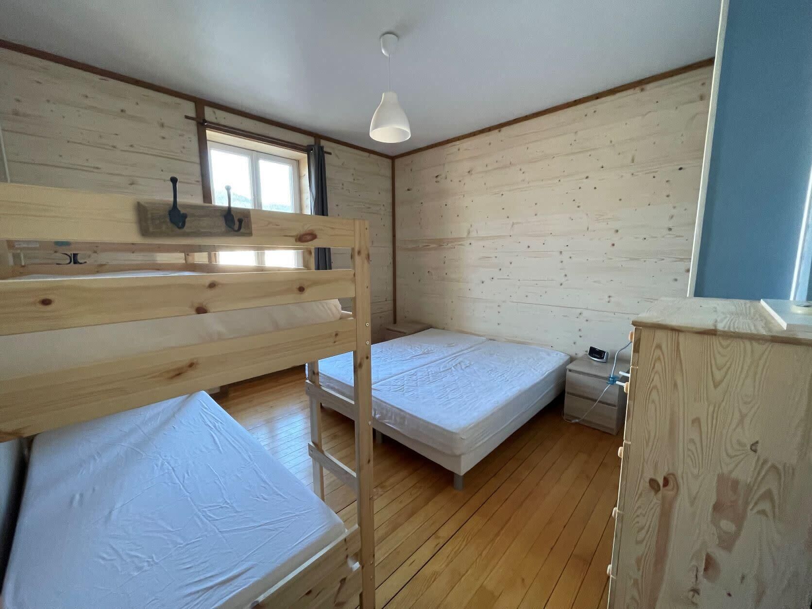 A room with wooden bunk beds, a single bed, a bedside table, a nightstand, and a window.