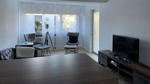 A modern living room with a large TV, a sofa, two armchairs, and a dining table. - Apartment in Alsdorf - near Aachen (Alsdorf)