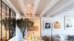 Un coin repas avec une table en bois dressée pour quatre personnes, entourée d’un grand miroir et d’une grande plante.