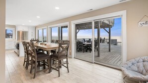 Een ruime keuken met een grote eettafel en stoelen, uitzicht op de oceaan door glazen schuifdeuren, en een terras met buitenmeubilair.