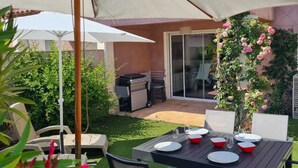 An outdoor patio with a table set for dining, surrounded by chairs and umbrellas, and a garden with climbing roses.