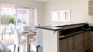 A modern kitchen with a black countertop, wooden cabinets, and a dining area with white chairs and a table.