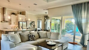 A spacious living room with a sectional sofa, a coffee table, and a view of a pool and garden. - The Ultimate Luxury 4 BR/3 BA, Heated Pool, Outdoor Kitchen (Port Charlotte)