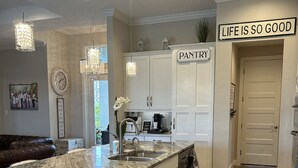 A modern kitchen with a marble island, white cabinetry, and a sign reading "LIFE IS SO GOOD". - The Ultimate Luxury 4 BR/3 BA, Heated Pool, Outdoor Kitchen (Port Charlotte)