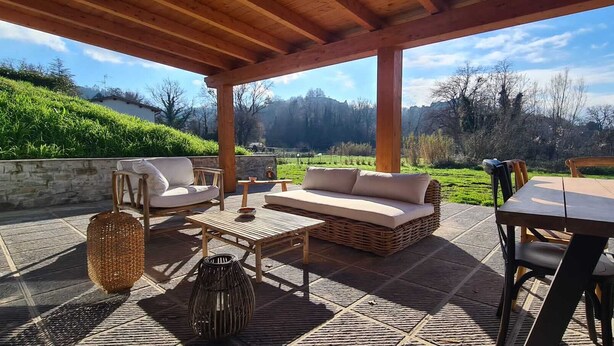 Un patio exterior con una pérgola de madera, un sofá, una mesa y sillas.