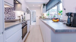 Uma cozinha moderna com armários brancos, painel de azulejos em padrão herringbone e forno embutido.