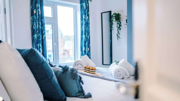 Quarto de hotel moderno com cama, almofadas, mesa de cabeceira e janela com cortinas.