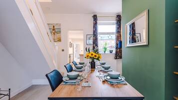 A dining room with a wooden table set for six, surrounded by chairs, with a vase of sunflowers on the table.
