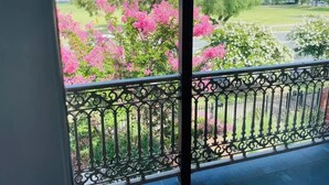 Un balcón con barandilla de hierro forjado que da a un jardín con árboles de flores rosadas.