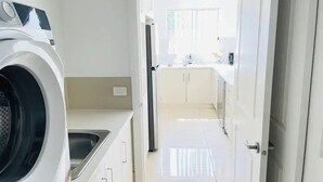 Un área de lavandería con lavadora, lavamanos y una cocina al fondo.