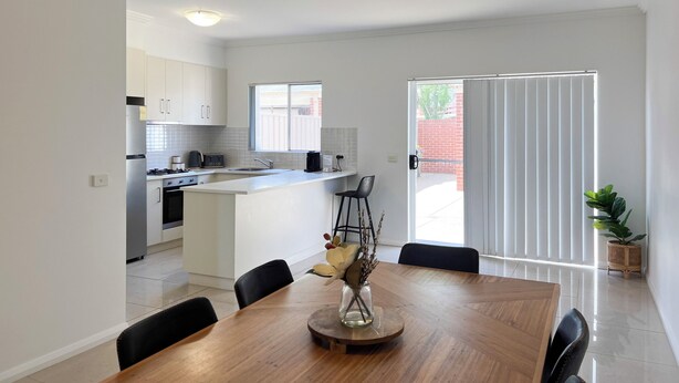 Una cocina moderna con armarios blancos, una isla central y un comedor con mesa y sillas de madera.