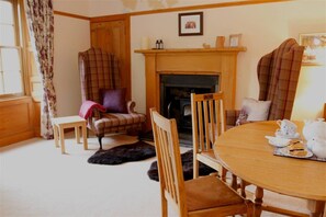 A cozy room with a fireplace, plaid chairs, a wooden table with tea set, and a fur rug. - Traditional Scottish Cottage (Blairgowrie)