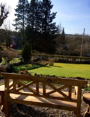 A wooden bench in a garden with a view of a lawn and trees. - Traditional Scottish Cottage (Blairgowrie)