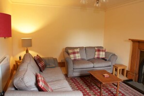 A living room with a sofa, a coffee table, a lamp, and a patterned rug. - Traditional Scottish Cottage (Blairgowrie)