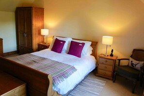 A bedroom with a wooden bed, two bedside tables with lamps, a wooden wardrobe, and a chair with a cushion. - Traditional Scottish Cottage (Blairgowrie)