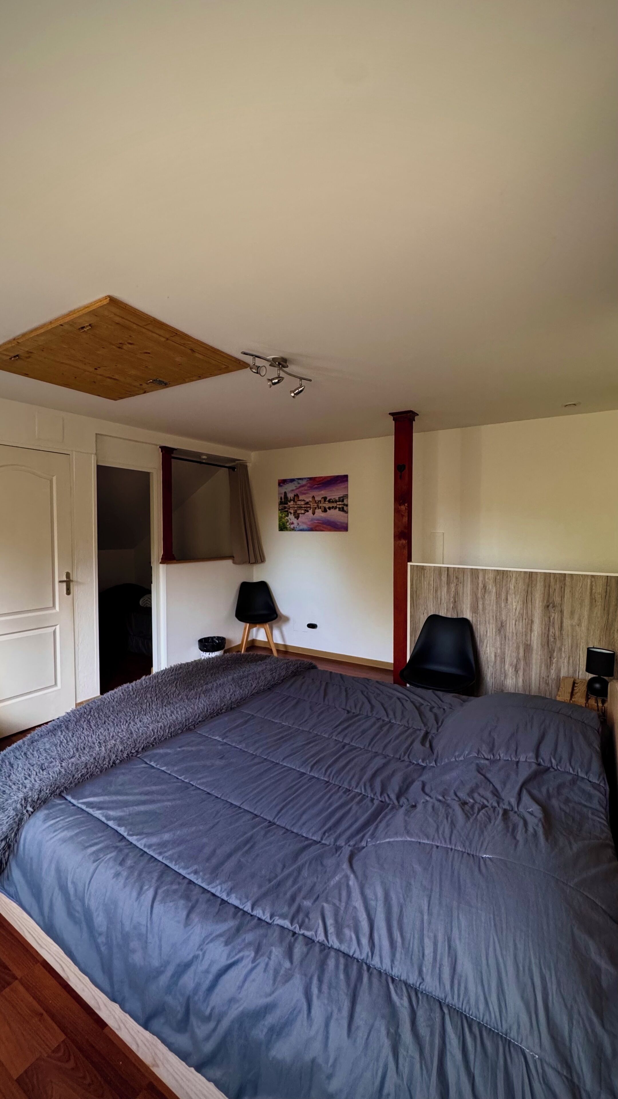Een slaapkamer met een groot bed, houten plafond, een schilderij en een rode accentmuur.