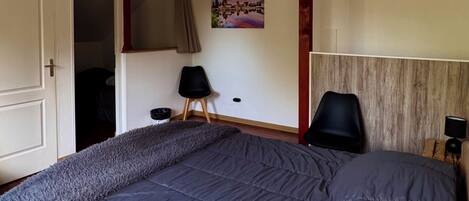 Een slaapkamer met een groot bed, houten plafond, een schilderij en een rode accentmuur.