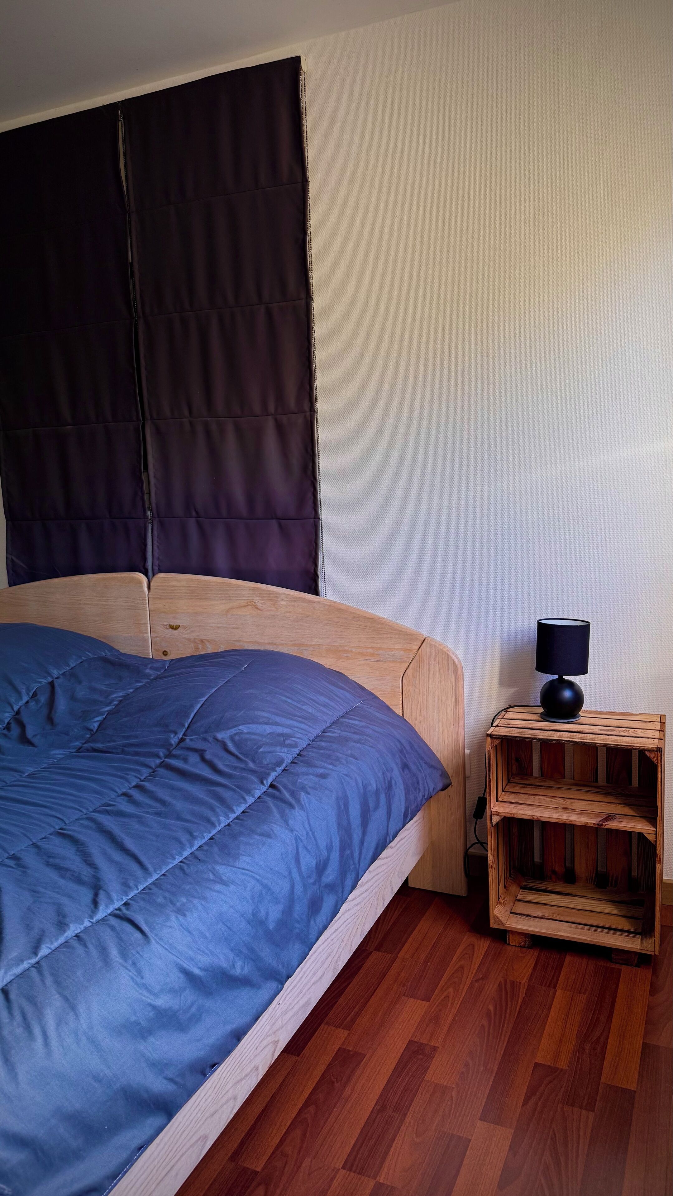 Un dormitorio con una cama, una mesita de noche de madera y una lámpara de pared.