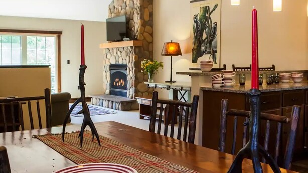 Un comedor con una mesa de madera preparada para cuatro personas, una chimenea y una pared de piedra.