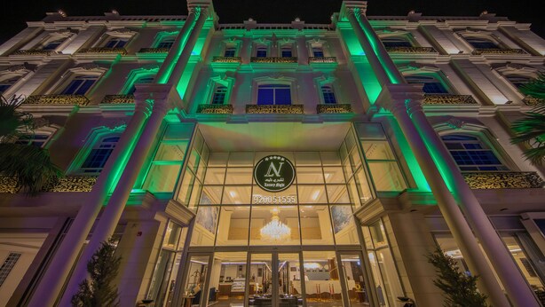 A grand hotel entrance with a large sign, columns, and a chandelier. - Luxury Night Al Munsiyah (Riyadh)