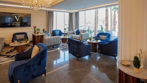 A spacious living area with modern furniture, a chandelier, and large windows offering a view of palm trees. - Luxury Night Al Munsiyah (Riyadh)