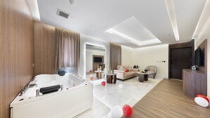 A modern hotel room with a large white bathtub, a sofa, a coffee table, and a TV. - Luxury Night Al Munsiyah (Riyadh)