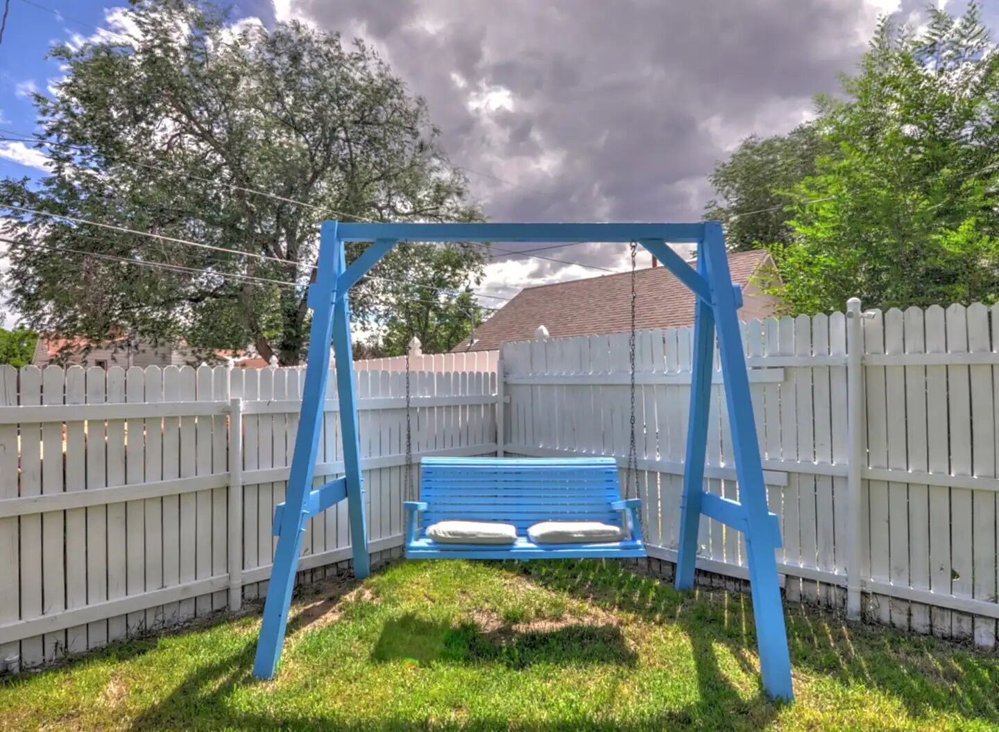 A backyard with a blue swing set and a white picket fence.