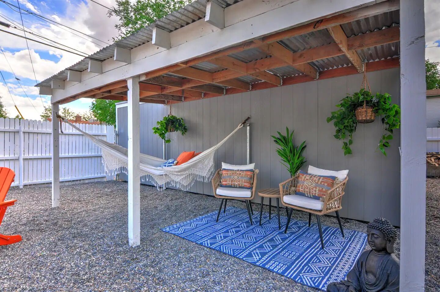 A covered outdoor seating area with a hammock, wicker chairs, and a Buddha statue.