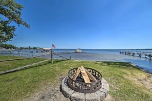 Vista a la orilla de un lago con una zona de fuego, muelle y barcos.