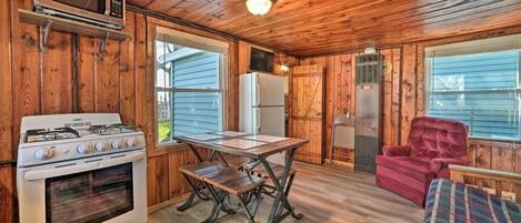 A wooden cabin interior with a kitchen area including a stove, microwave, refrigerator, and a dining table with benches.