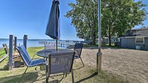 A beachside patio with a table and chairs, a covered umbrella, and a view of the water. - Full Cabin: 14 Steps to the Lake!  PET FRIENDLY! (Houghton Lake)
