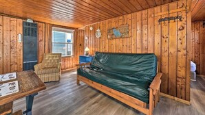 A wooden cabin interior with a green sofa, a wicker chair, and a small table. - Full Cabin: 14 Steps to the Lake!  PET FRIENDLY! (Houghton Lake)