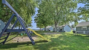 A playground with a slide and a swing set, surrounded by trees and a view of houses. - Full Cabin: 14 Steps to the Lake!  PET FRIENDLY! (Houghton Lake)