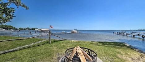 A lakeside view with a fire pit, dock, and boats.