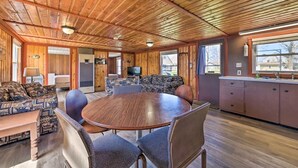 Ein gemütliches Blockhaus-Interieur mit Holzbalkendecke, einem runden Esstisch und einer Küchenzeile mit Schränken und Spüle.