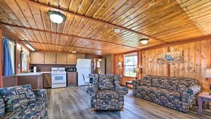Ein Interieur einer Holzhütte mit Holzbalkendecke, einer Küchenzeile, einem gemusterten Sofa und einem gemusterten Sessel.