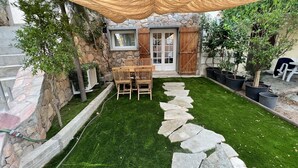 Un espace patio agrémenté d’un mur en pierre, d’une table et de chaises en bois, et d’un chemin en pierre.