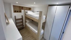 Une chambre avec un lit superposé, une échelle en bois, une petite étagère avec des objets décoratifs et une armoire.