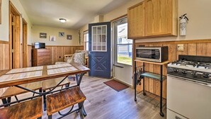 A compact kitchen with wooden cabinets, a microwave, a gas stove, and a dining table with benches. - Full Cabin: Steps to the Lake!  PET FRIENDLY! (Houghton Lake)