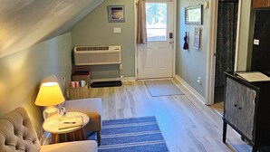 Ein gemütliches Schlafzimmer im Dachgeschoss mit einem Bett, einem kleinen Tisch mit einer Lampe, einem Sessel, einer Kommode und einer Tür, die auf einen Balkon führt.