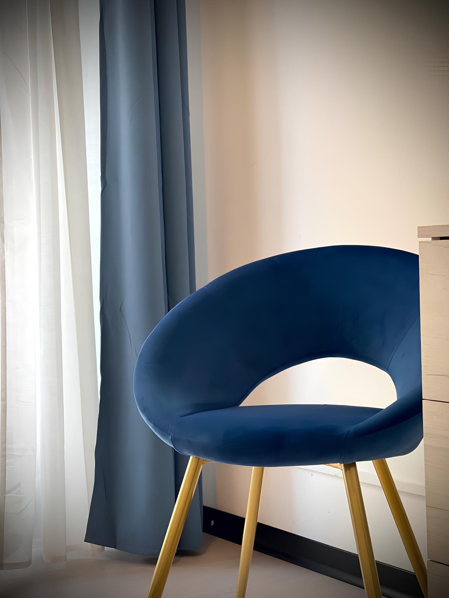 A blue chair with a unique design, positioned in a room with a light-colored floor and a wooden cabinet to the right.