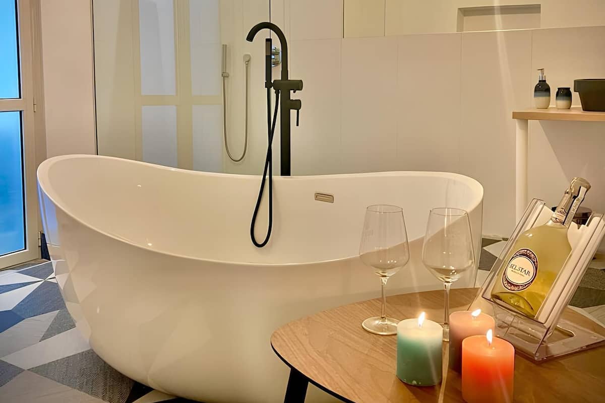 A modern bathroom with a freestanding bathtub, a glass shower enclosure, and a small table with candles and a bottle of alcohol.