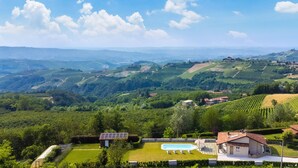 Eine Villa mit Schwimmbad, umgeben von üppiger Vegetation und Weinbergen, mit Blick über ein Tal.
