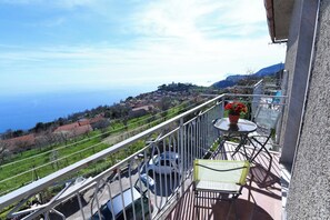 A balcony with a view of a coastal town, a table with a potted plant, and a chair. - House on 3 levels, with wide sea views. (Agerola)
