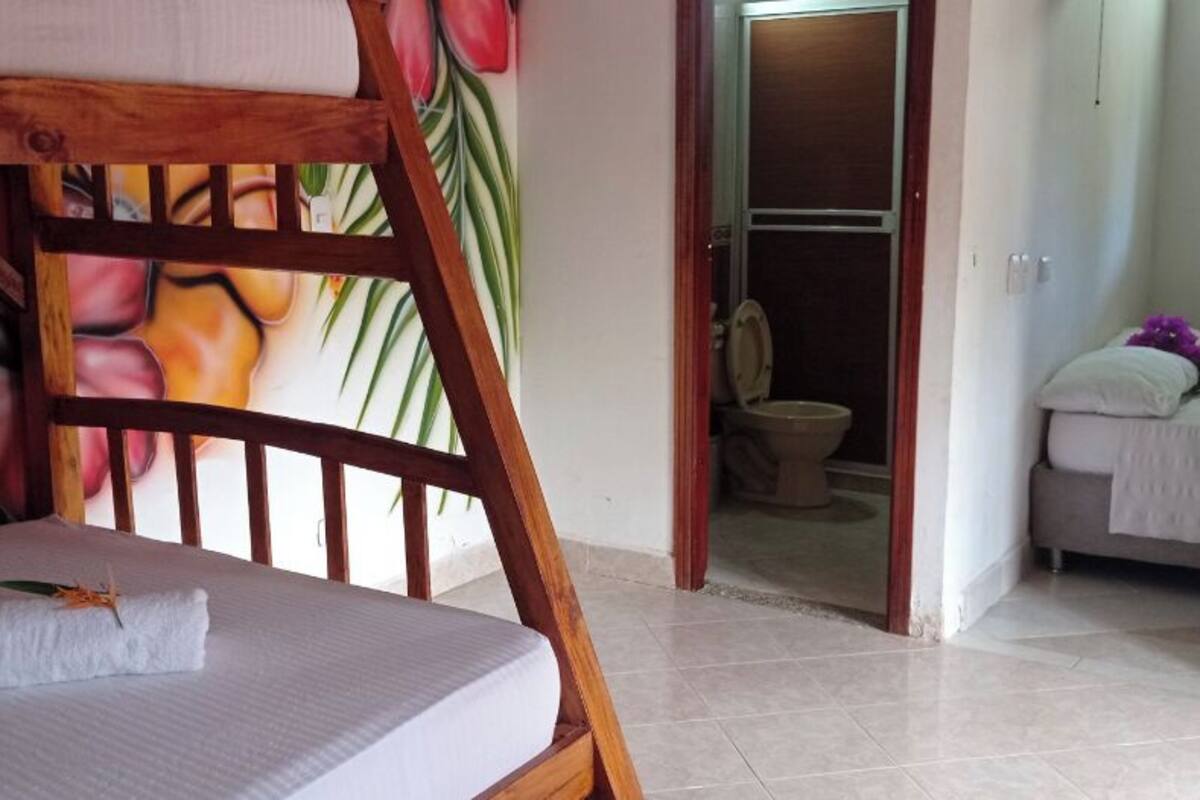 Una habitación con una cama litera, un baño con inodoro y cama, y una puerta que da a otra habitación.