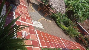 Une terrasse carrelée agrémentée d’un jardinier en pierre, d’une petite statue et de diverses plantes.