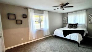 Une chambre à coucher avec un lit, un ventilateur de plafond et une fenêtre avec des rideaux.