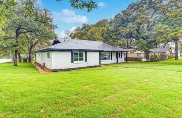 A single-story house with a gabled roof, surrounded by a well-maintained lawn and trees. - Spacious Dallas Home! Minutes from AT&T Stadium. Groups welcome (Fort Worth)