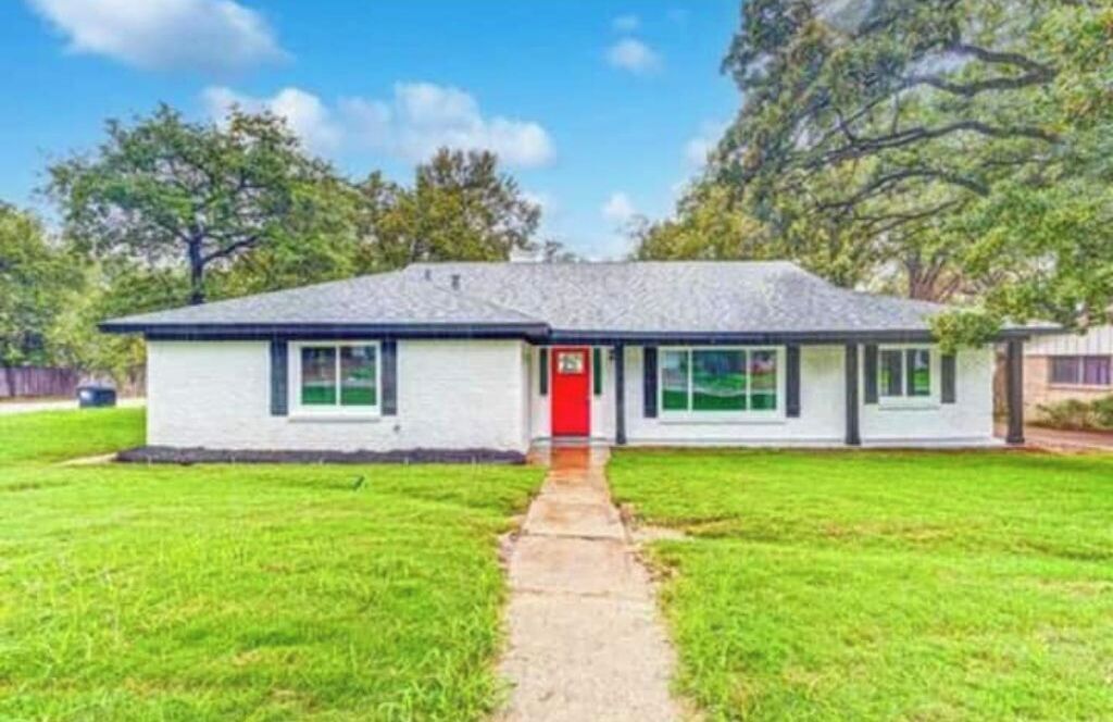 A single-story house with a red door, white exterior, and a small front yard.