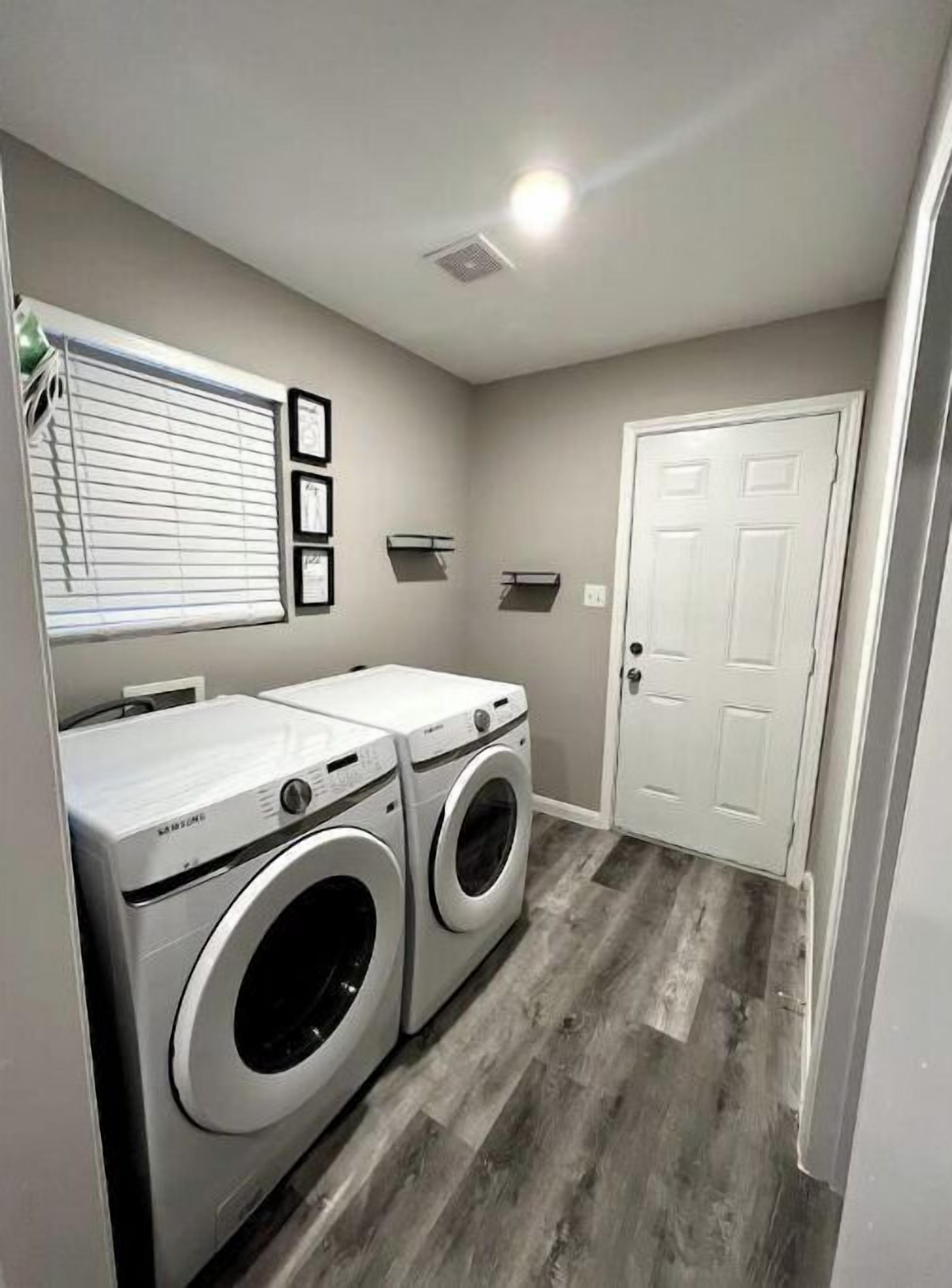 A laundry room with two front-loading washers, a white door, and a window with blinds.
